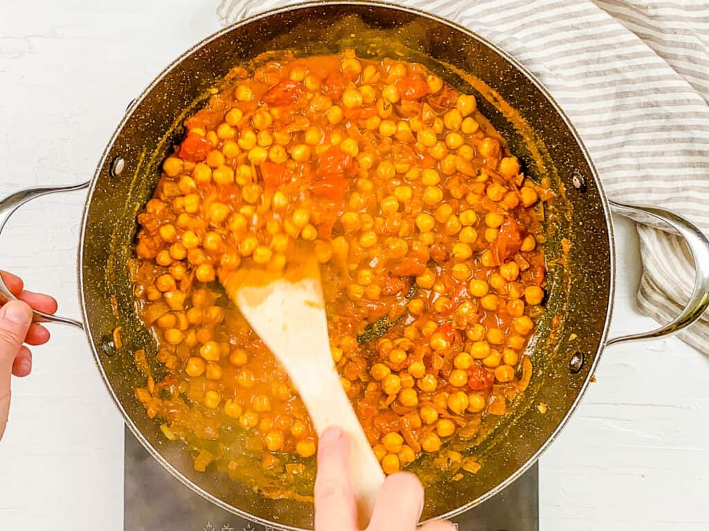 Vegan chana masala cooking in a large pot on the stove.