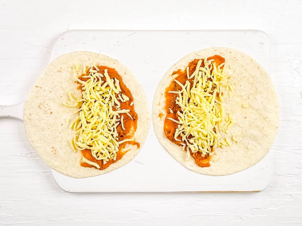Tortillas topped with refried beans and cheese on a cutting board.