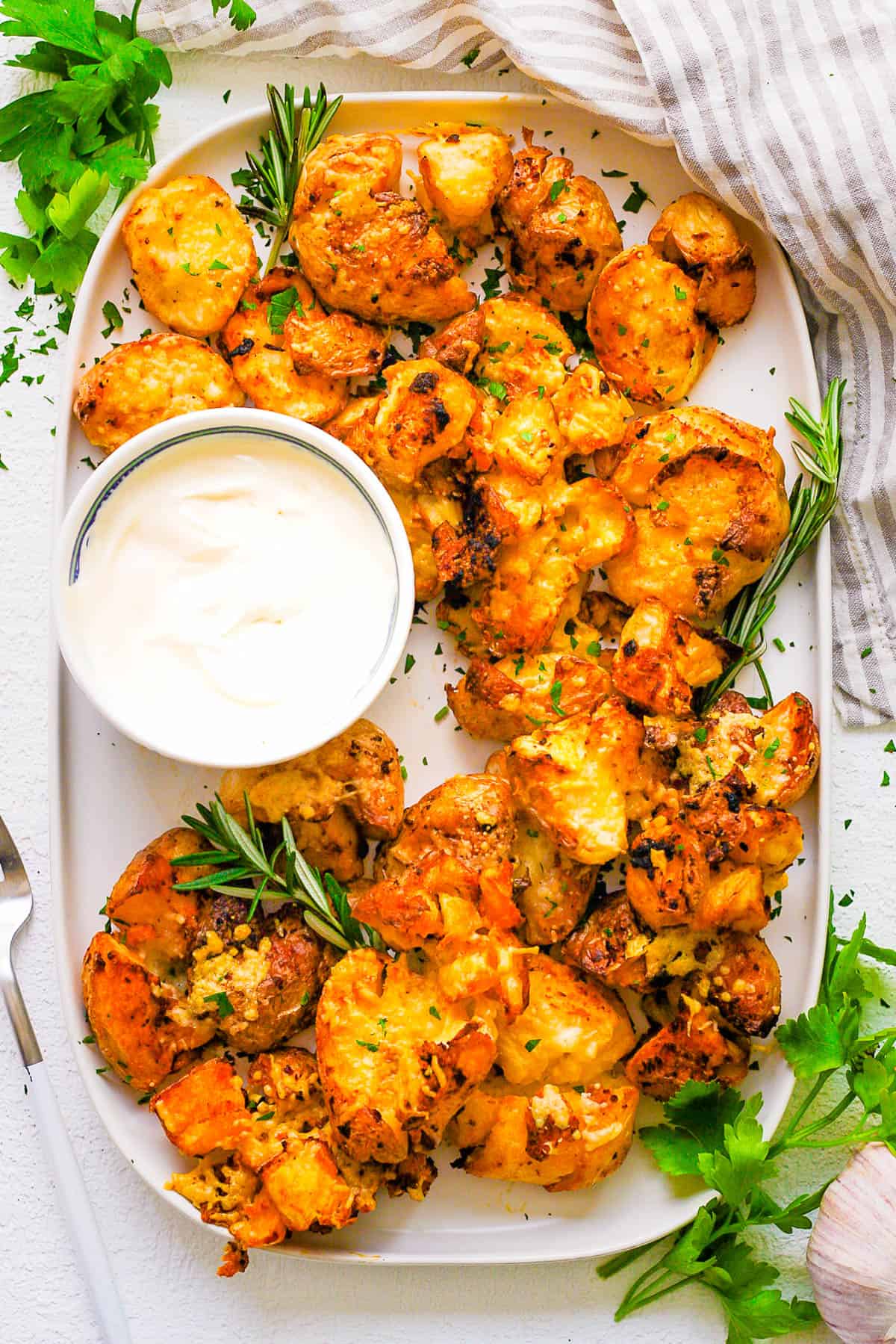 Air fryer smashed potatoes served on a white tray with dipping sauce on the side.