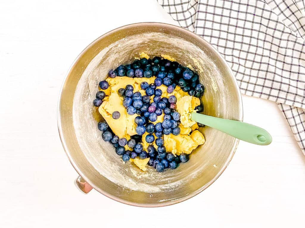 Blueberries added to lemon sugar cookie dough in a mixing bowl.