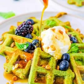 Healthy green waffles served on a white plate with fresh berries, whipped cream and maple syrup.