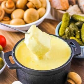 Vegan fondue with a cube of bread dipped into it, served in a fondue pot.