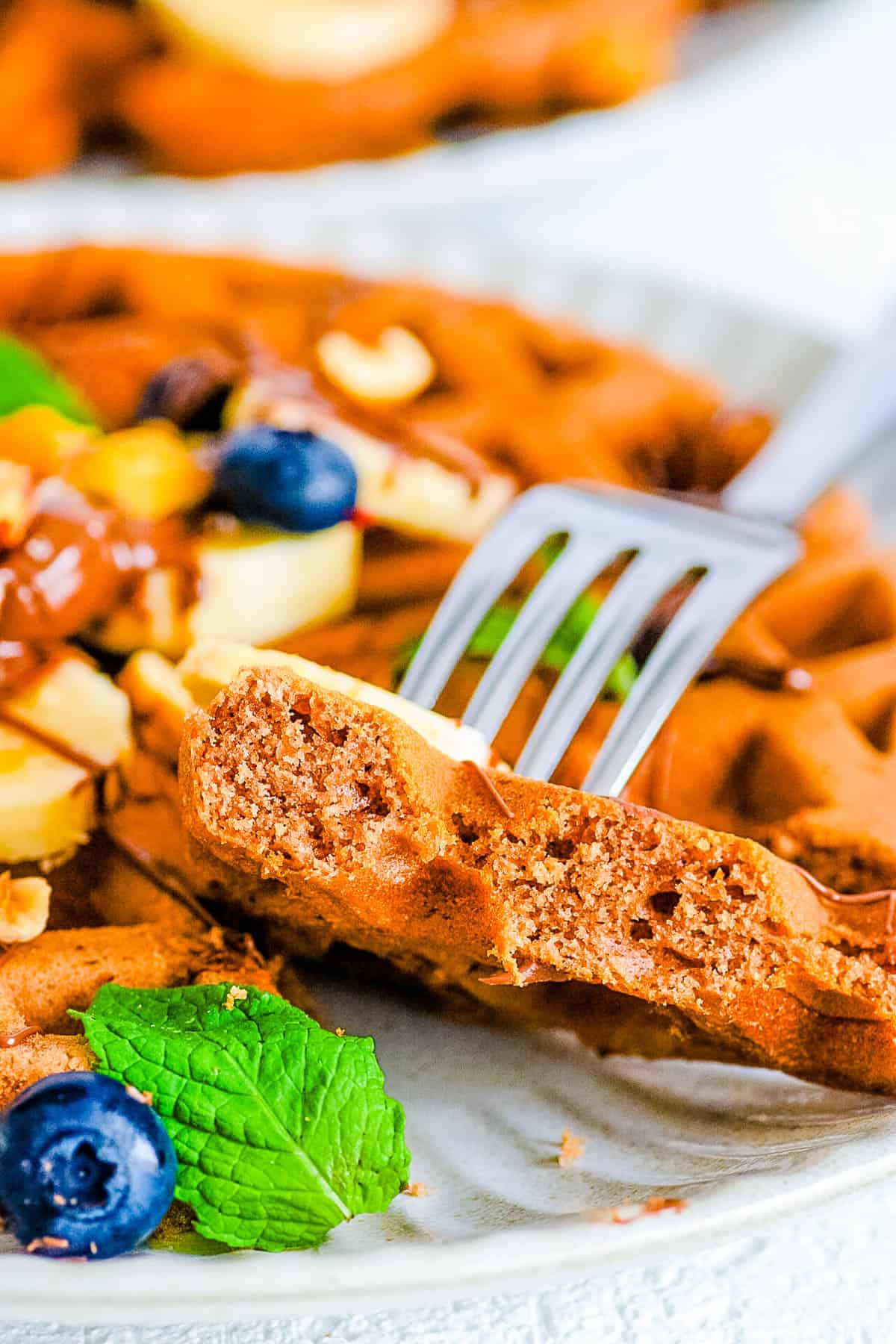 A forkful of easy nutella waffles topped with fresh berries, banana slices, and a drizzle of nutella sauce on top.