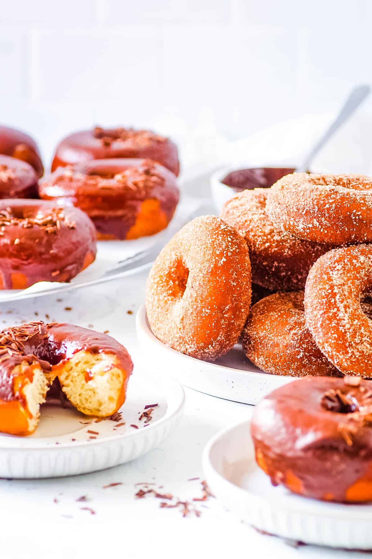 Eggless donuts served two ways - with a cinnamon sugar topping and with a c،colate glaze, served on a few white plates.