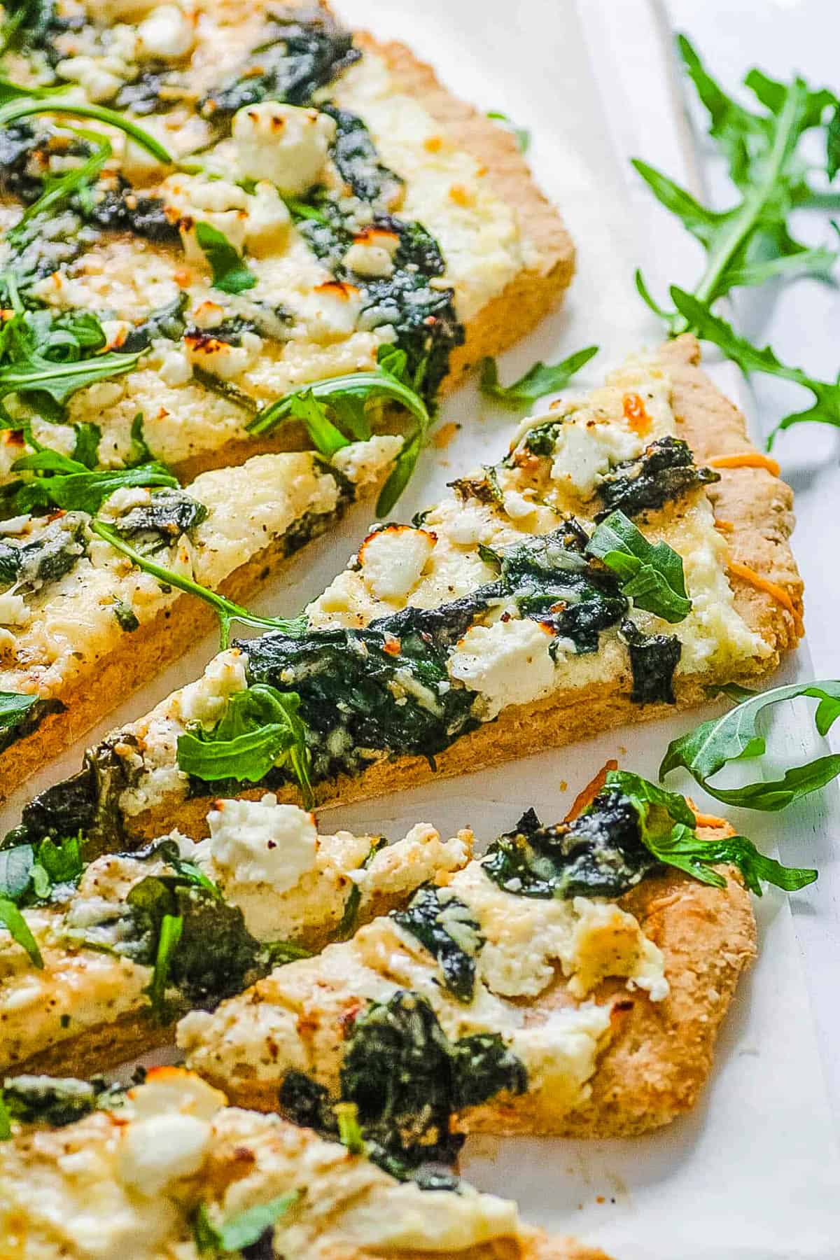 Spinach pizza with ricotta and feta cheese sliced on a white platter.