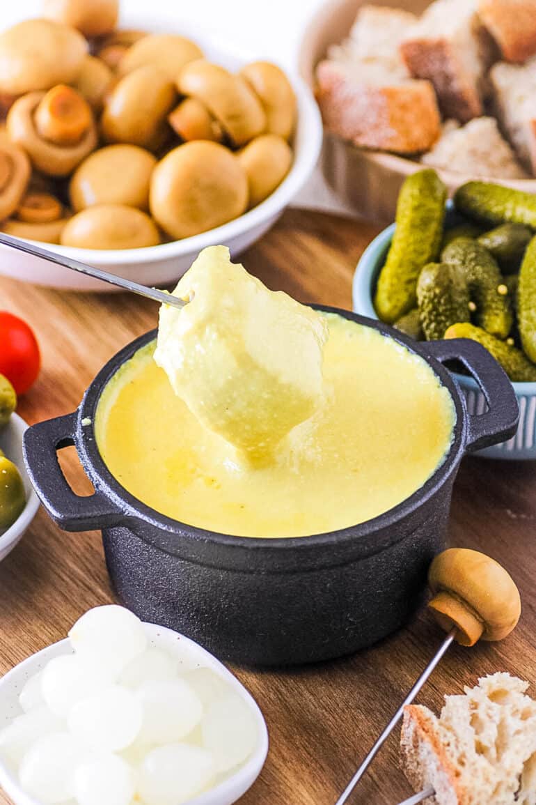 Vegan fondue with a cube of bread dipped into it, served in a fondue pot.
