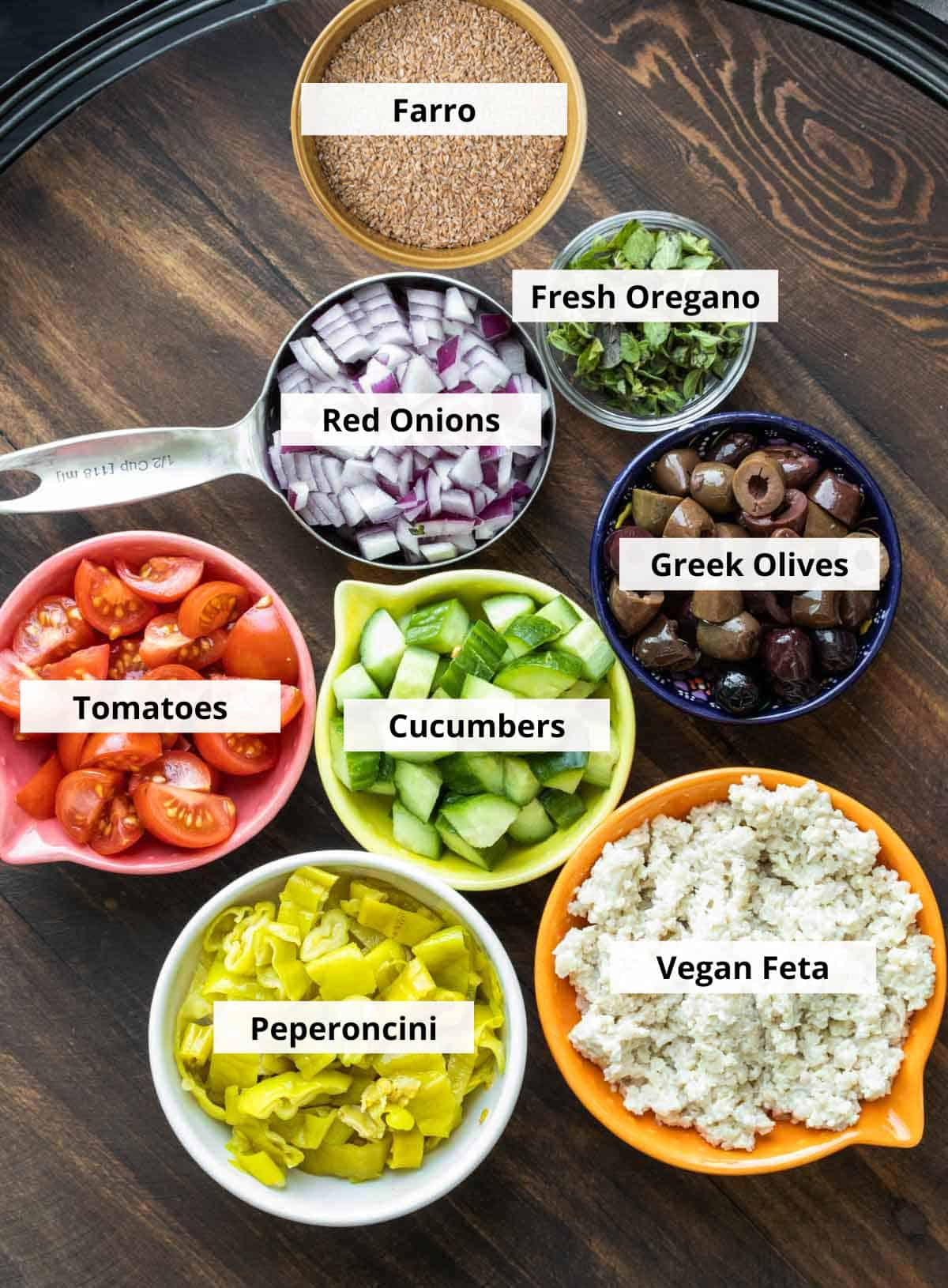 Ingredients for vegan farro salad recipe - like veggies and vegan feta - in bowls on a wooden table.