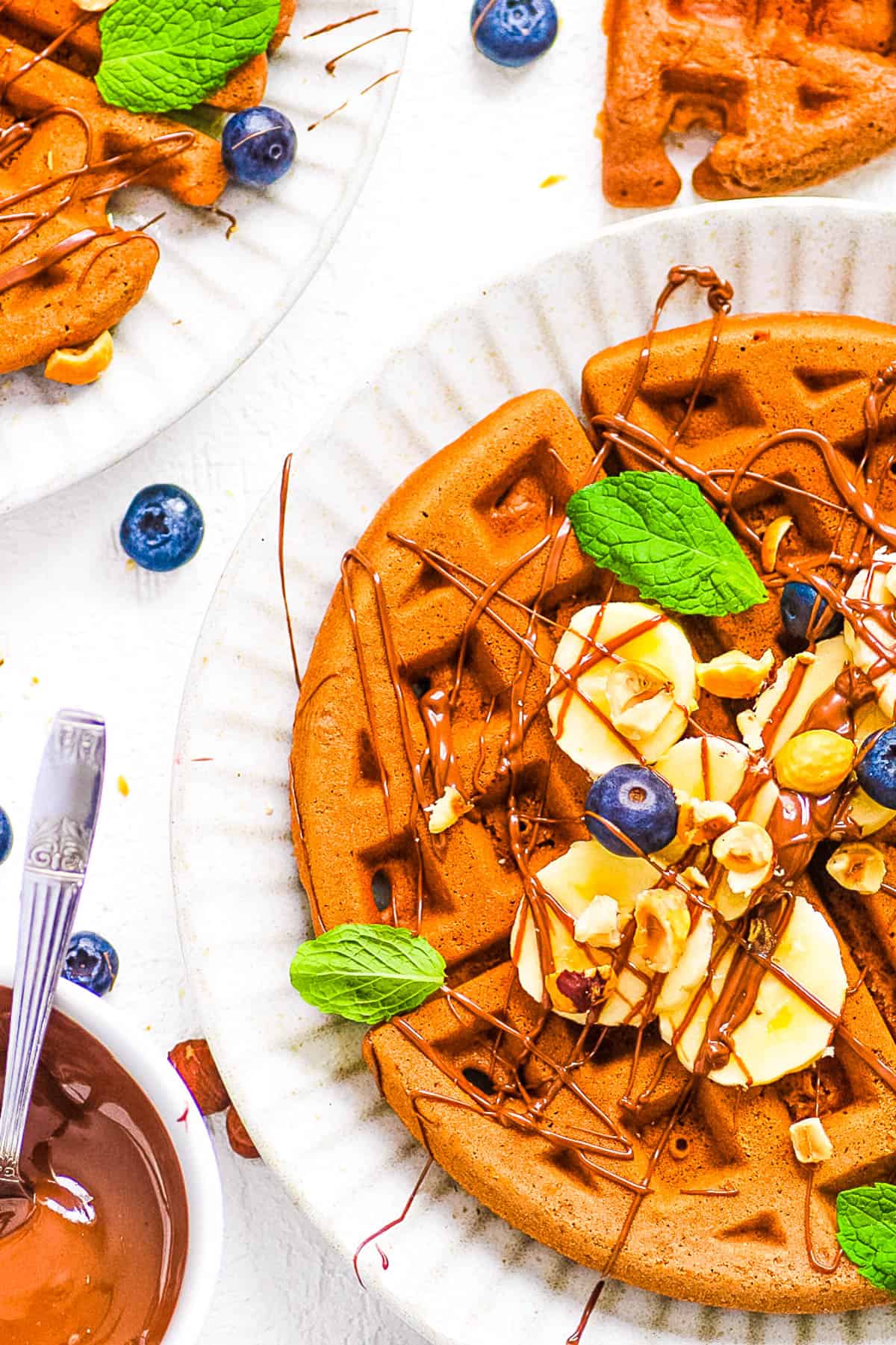 Nutella waffles topped with fresh berries, banana slices, and a drizzle of nutella sauce on top, served on a white plate.