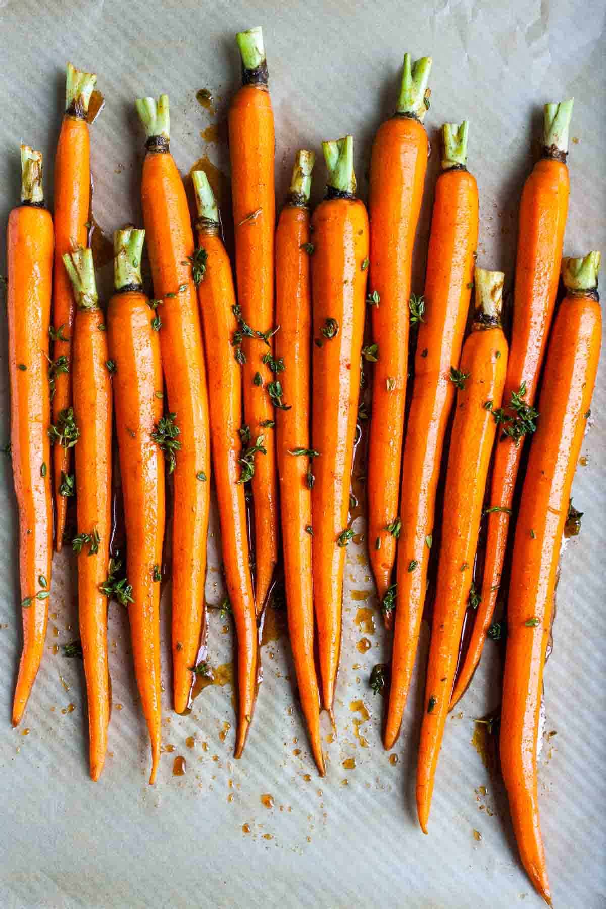 A group of carrots next to each other on a piece of parchment paper with herbs on them.