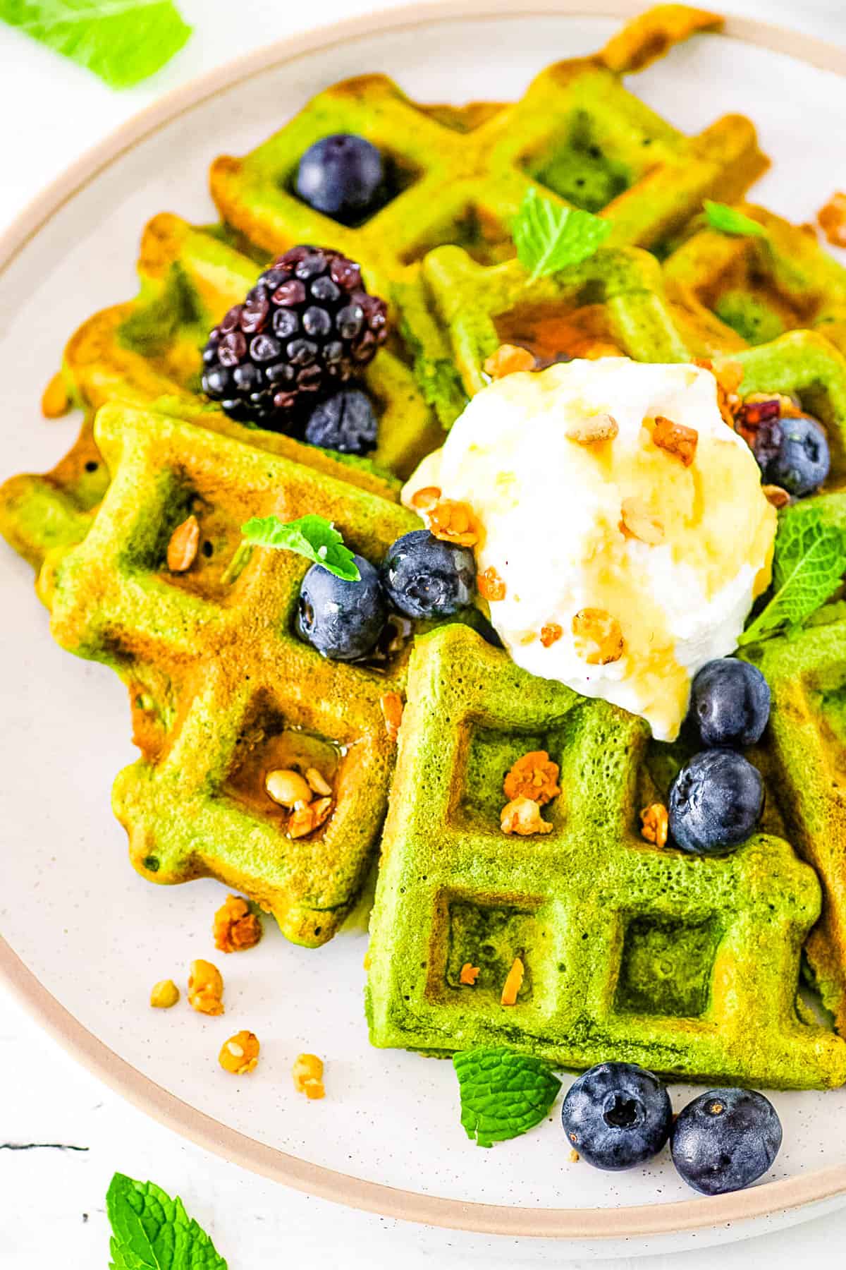 Healthy green waffles made in a blender, served on a white plate with fresh berries, whipped cream and maple syrup.