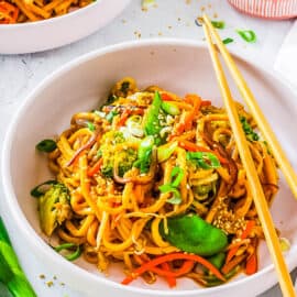 Healthy vegan chow mein noodles with vegetables served in a white bowl with chopsticks.