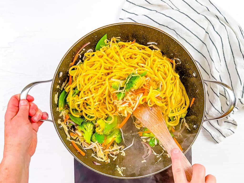 Vegan Chinese noodles being cooked in a pan with vegetables and sauce.