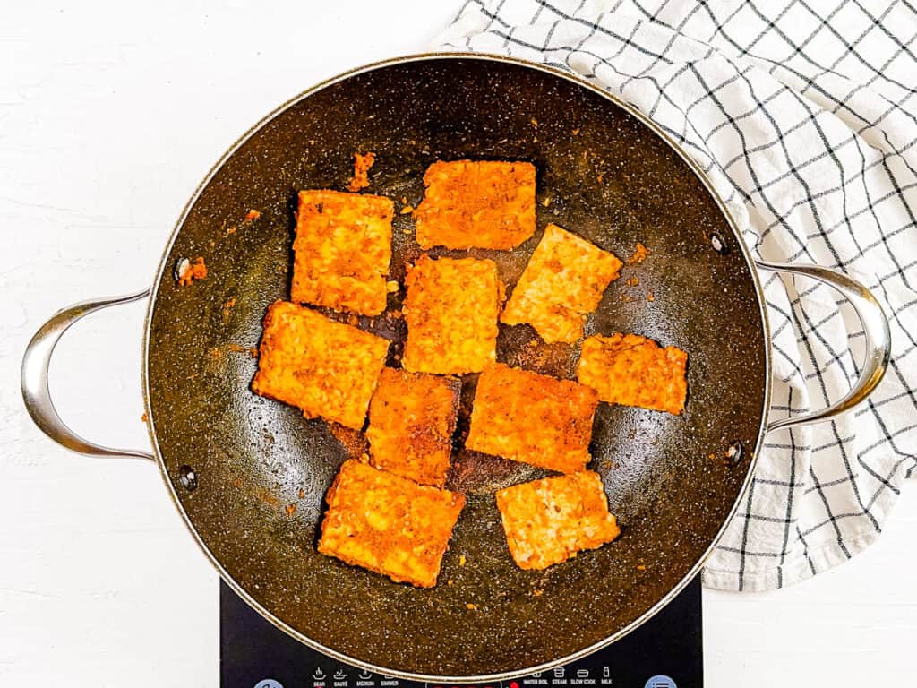 Marinated tempeh cooking in a skillet.