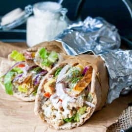 Two tempeh gyros rolled up in pita bread with veggies and covered in foil.