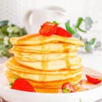 A tall stack of almond milk pancakes drizzled with maple syrup on a white plate.