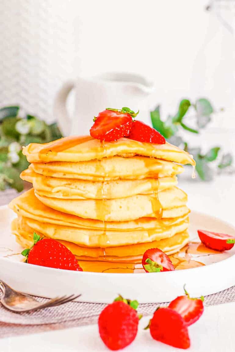 A tall stack of almond milk pancakes drizzled with maple syrup on a white plate.