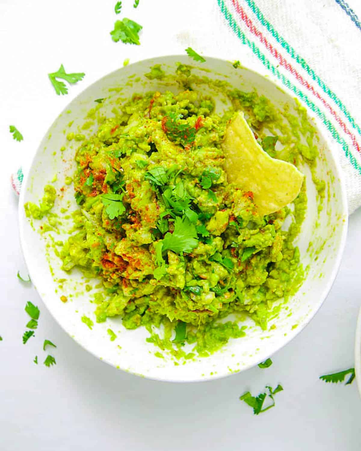 Healthy guacamole served in a bowl with a tortilla chip garnish.