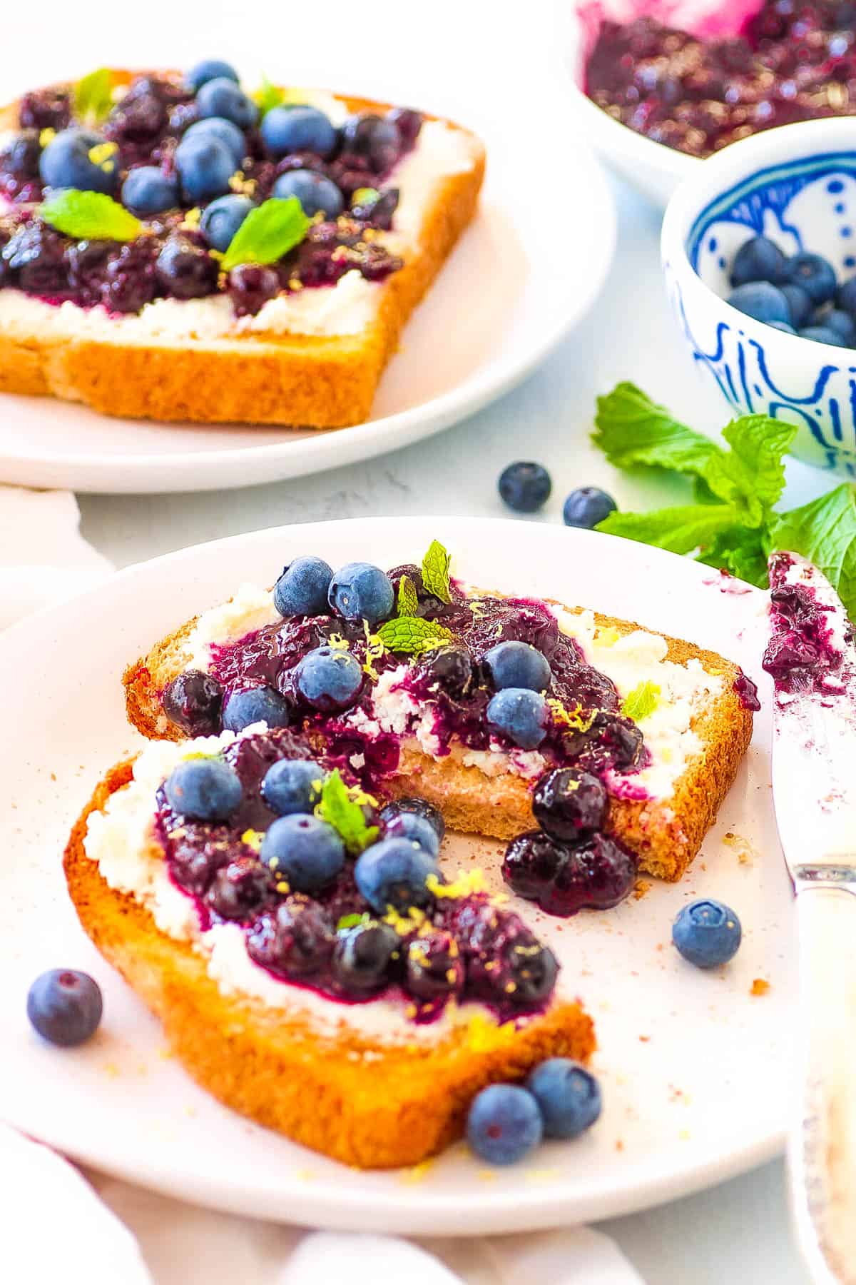 Blueberry cream cheese toast garnished with fresh mint, served on a white plate.