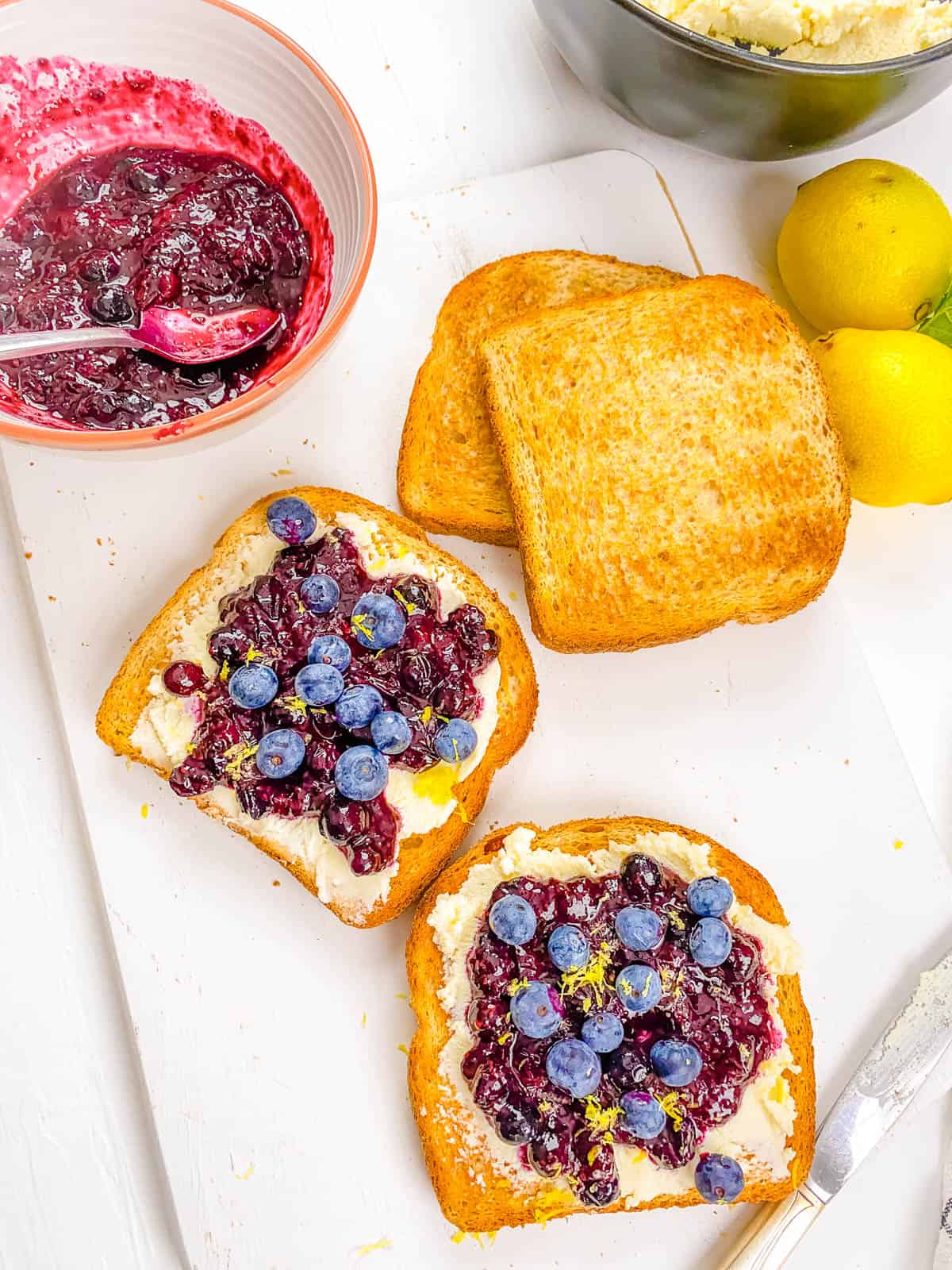 Cream cheese toast with blueberries (and 15 other topping ideas) on a white cutting board.