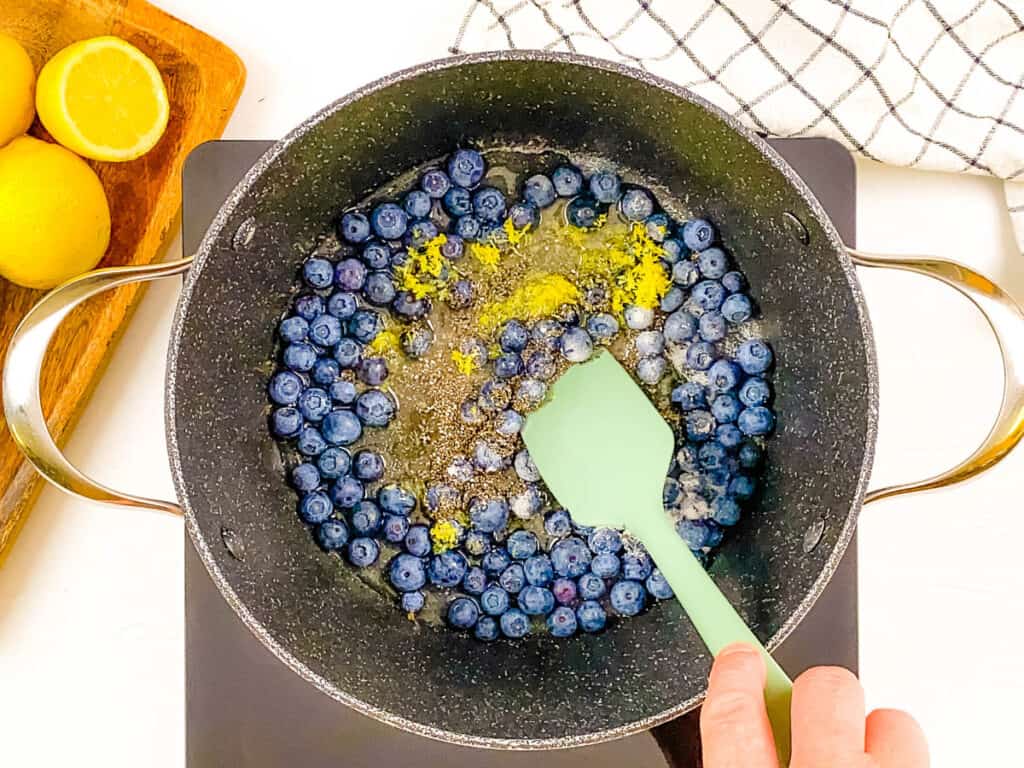 Blueberries and lemon zest cooking in a pot to make blueberry compote.