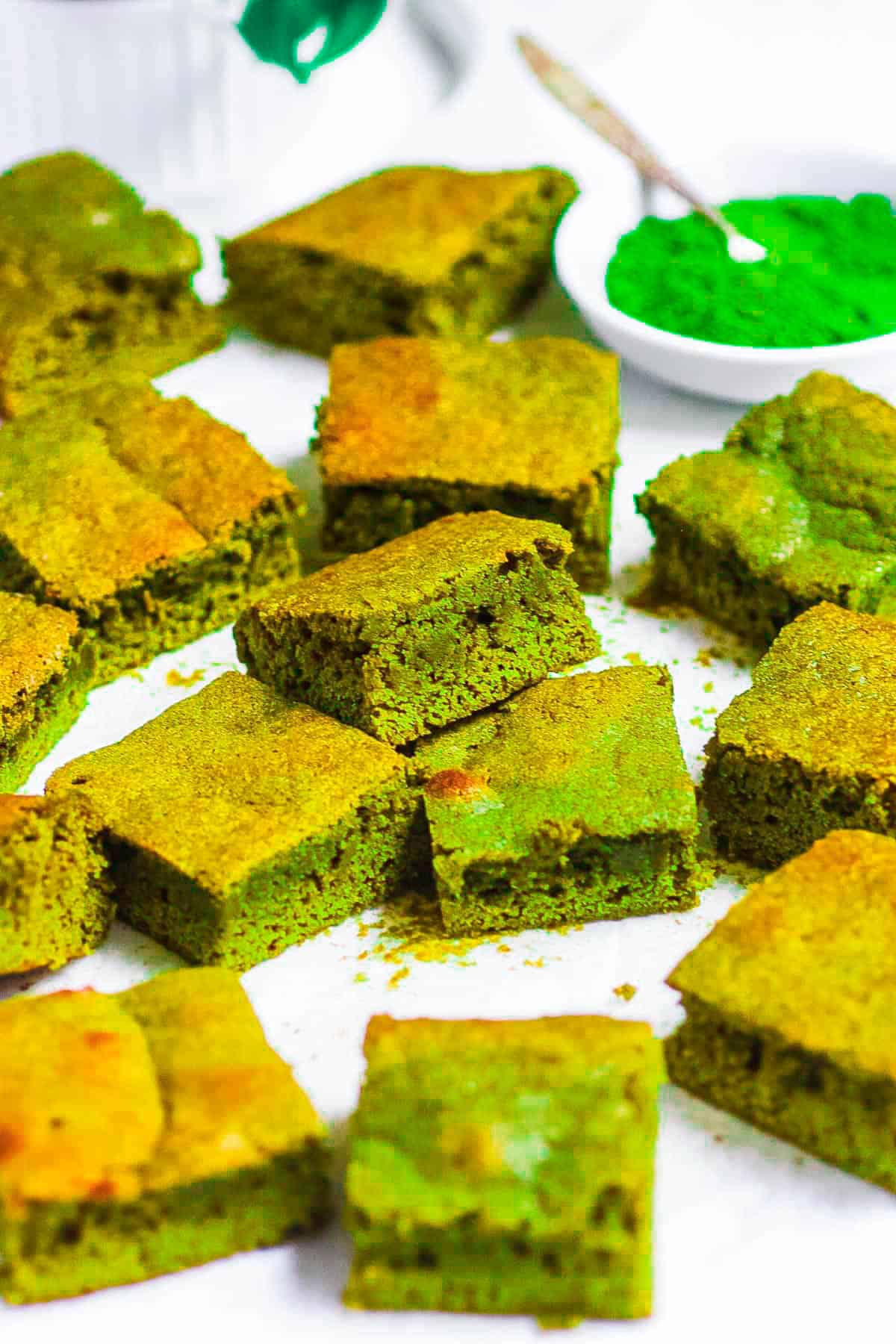 Matcha brownies stacked on white parchment paper on a countertop.