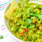 Low calorie healthy guacamole recipe served in a bowl with a tortilla chip garnish.