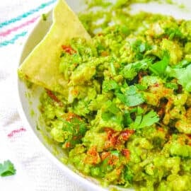 Low calorie healthy guacamole recipe served in a bowl with a tortilla chip garnish.