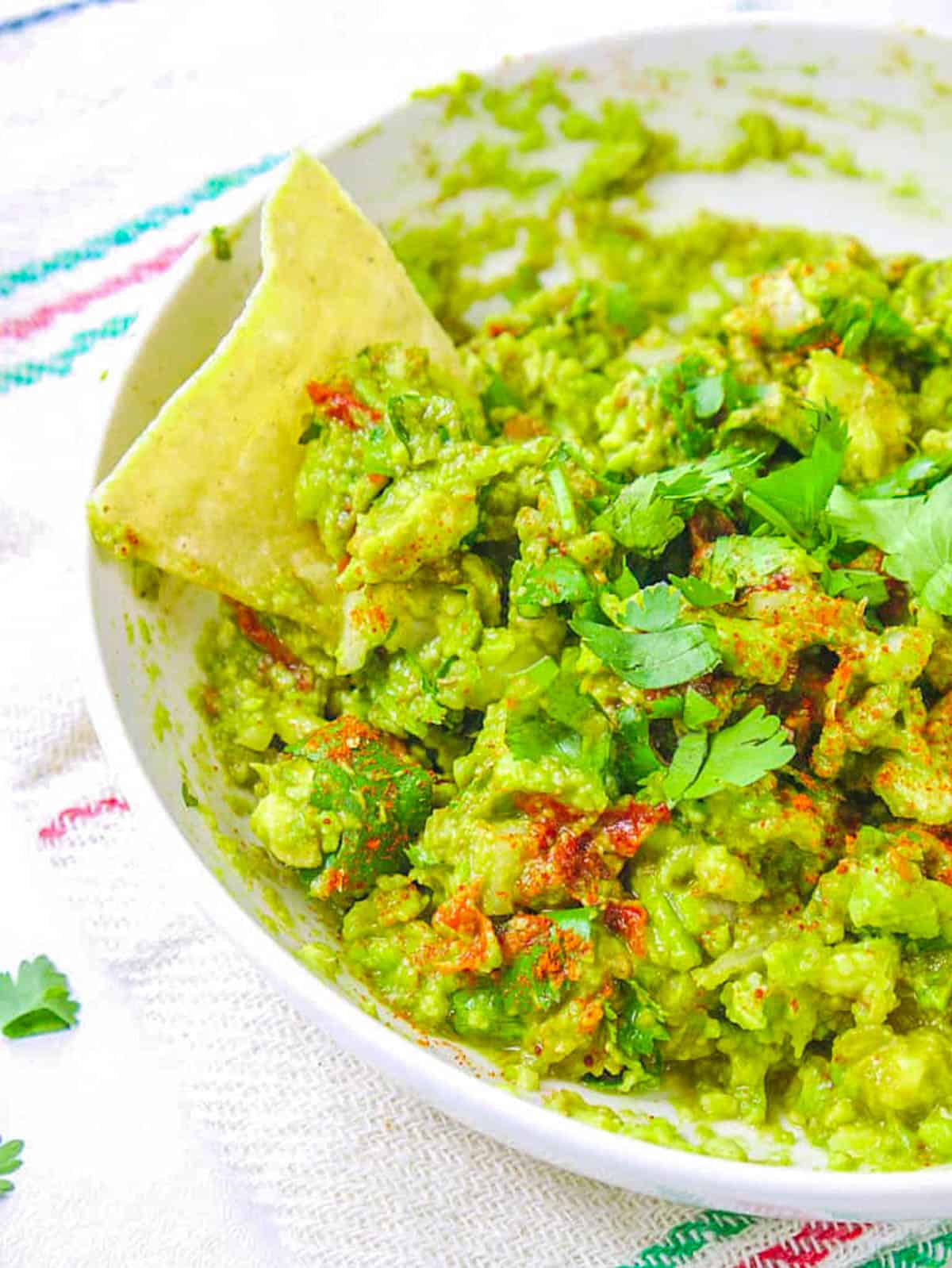 Low calorie healthy guacamole recipe served in a bowl with a tortilla chip garnish.