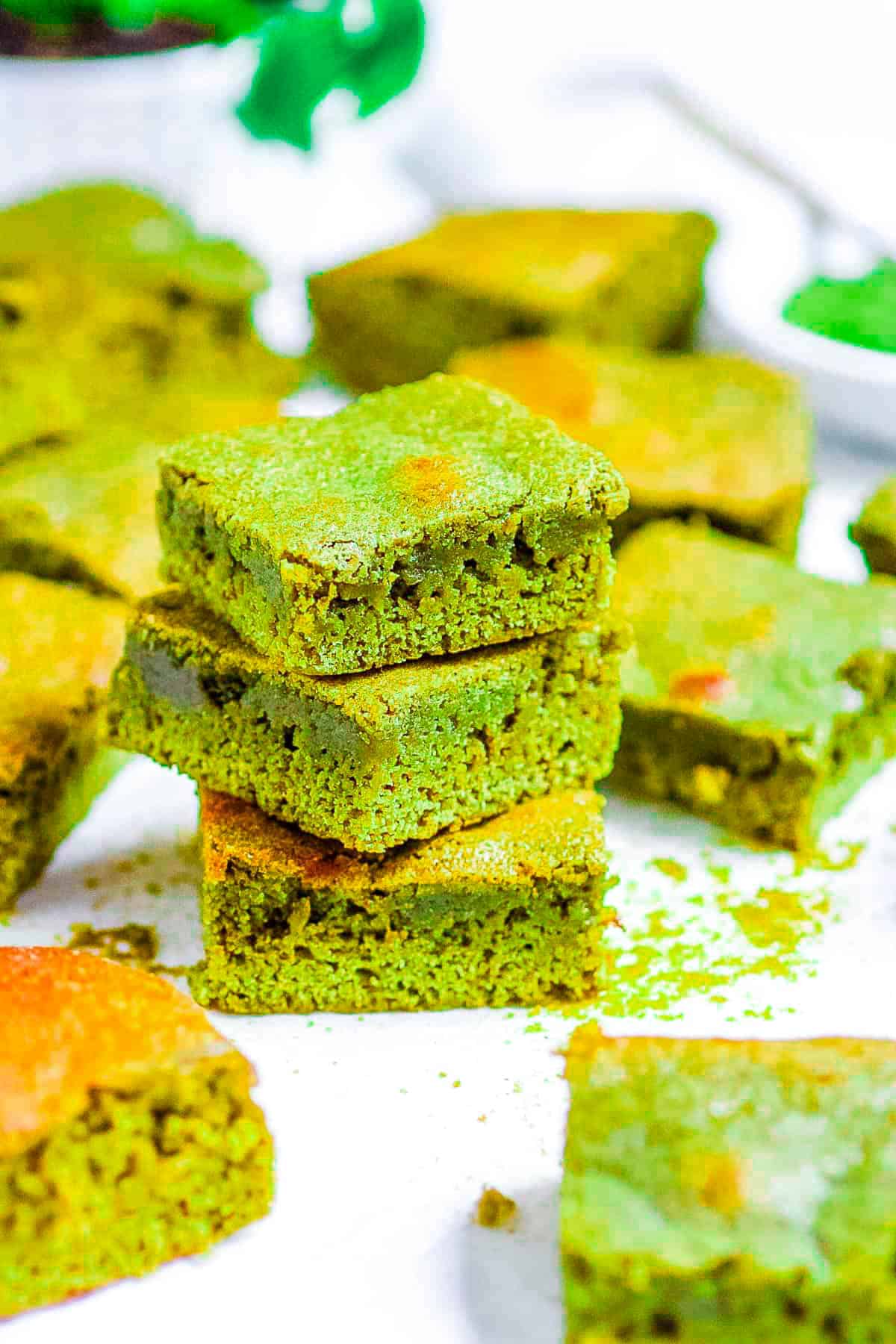 Matcha brownies stacked on white parchment paper on a countertop.