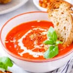 Three ingredient tomato soup with canned tomatoes served in a white bowl with fresh basil and crusty bread as a garnish.