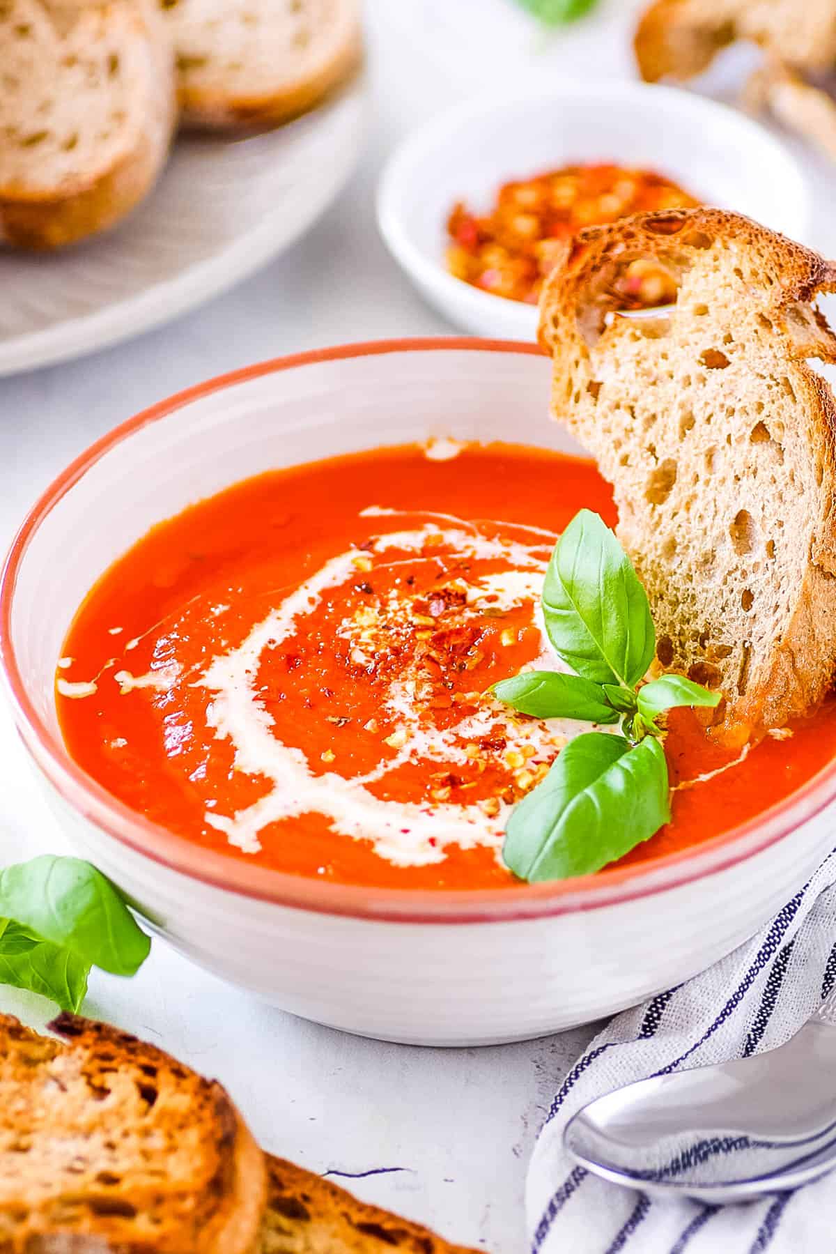 Soupe à la tomate à trois ingrédients avec des tomates en conserve servie dans un bol blanc avec du basilic frais et du pain croûté comme garniture.