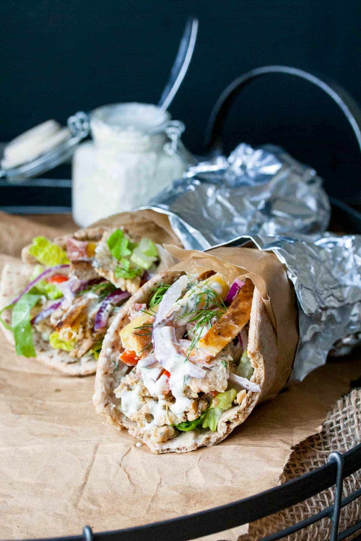 Two tempeh gyros rolled up in pita bread with veggies and covered in foil.