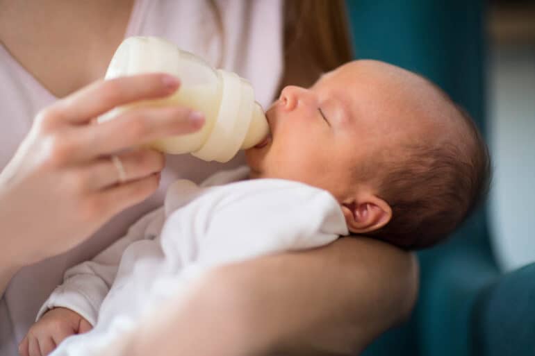 Close Up Of Loving Mother Feeding Newborn Baby Son With Bottle At Home.