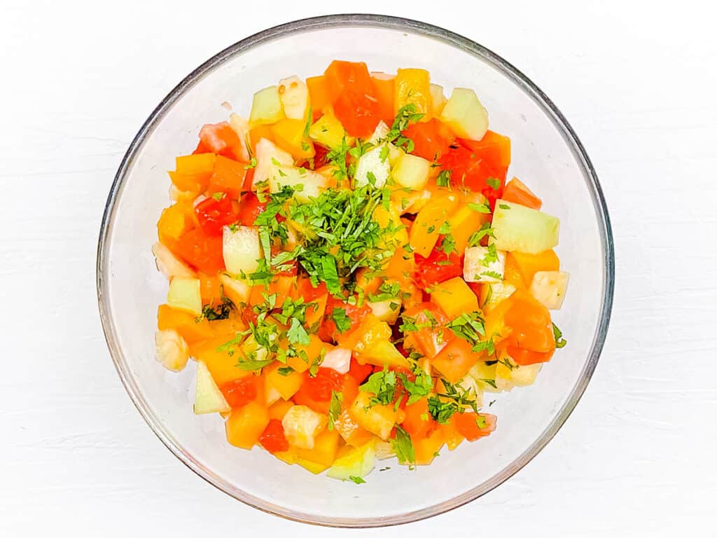Chili lime fruit salad tossed with fresh cilantro, salt, and pepper in a bowl.
