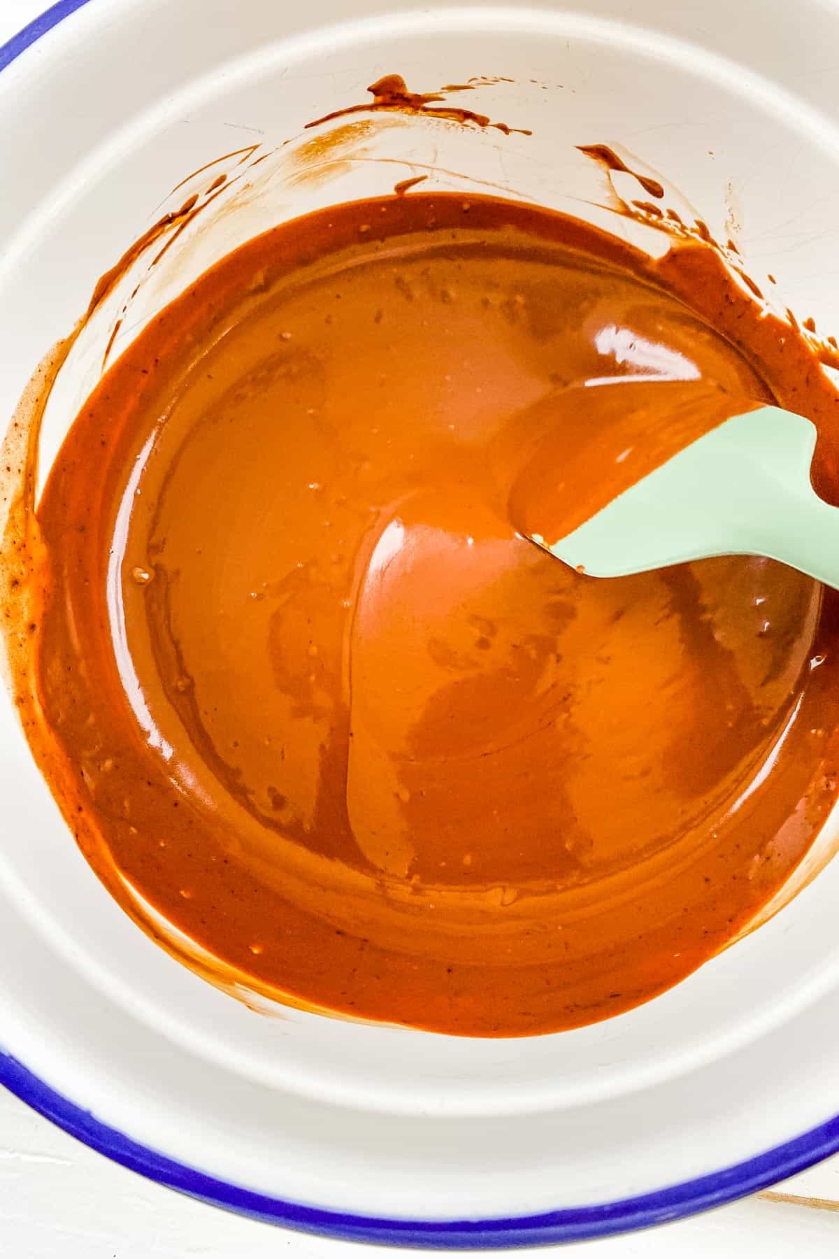 Smooth chocolate ganache frosting in a large white mixing bowl. 