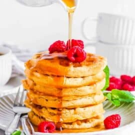 Gluten free vegan waffles stacked on a white plate, topped with raspberries and maple syrup.