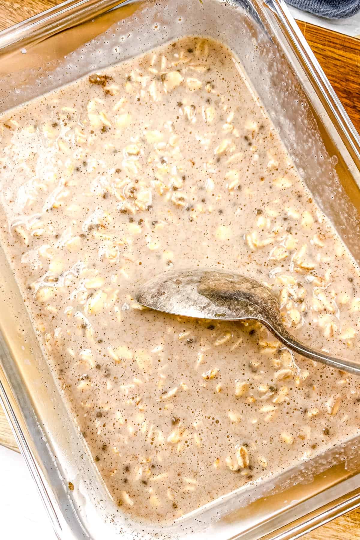 Oats soaking in a glass dish with a metal spoon. 
