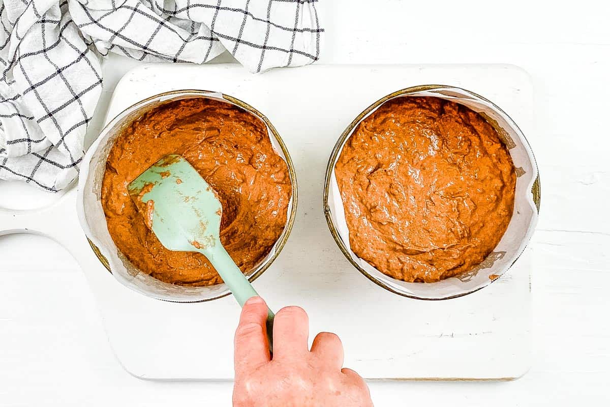 The cake batter is divided between two cake tins lined with parchment paper. 