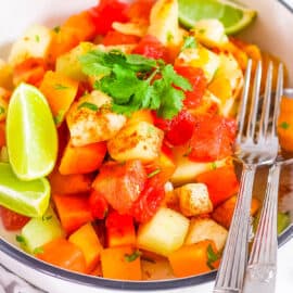 Mexican fruit salad with tajin seasoning, cilantro and fresh lime served in a bowl with a fork.