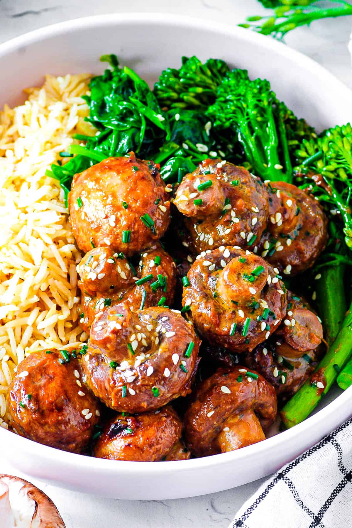 Miso mushrooms tossed with garlic miso ،er, served in a white bowl with brown rice and fresh greens on the side.