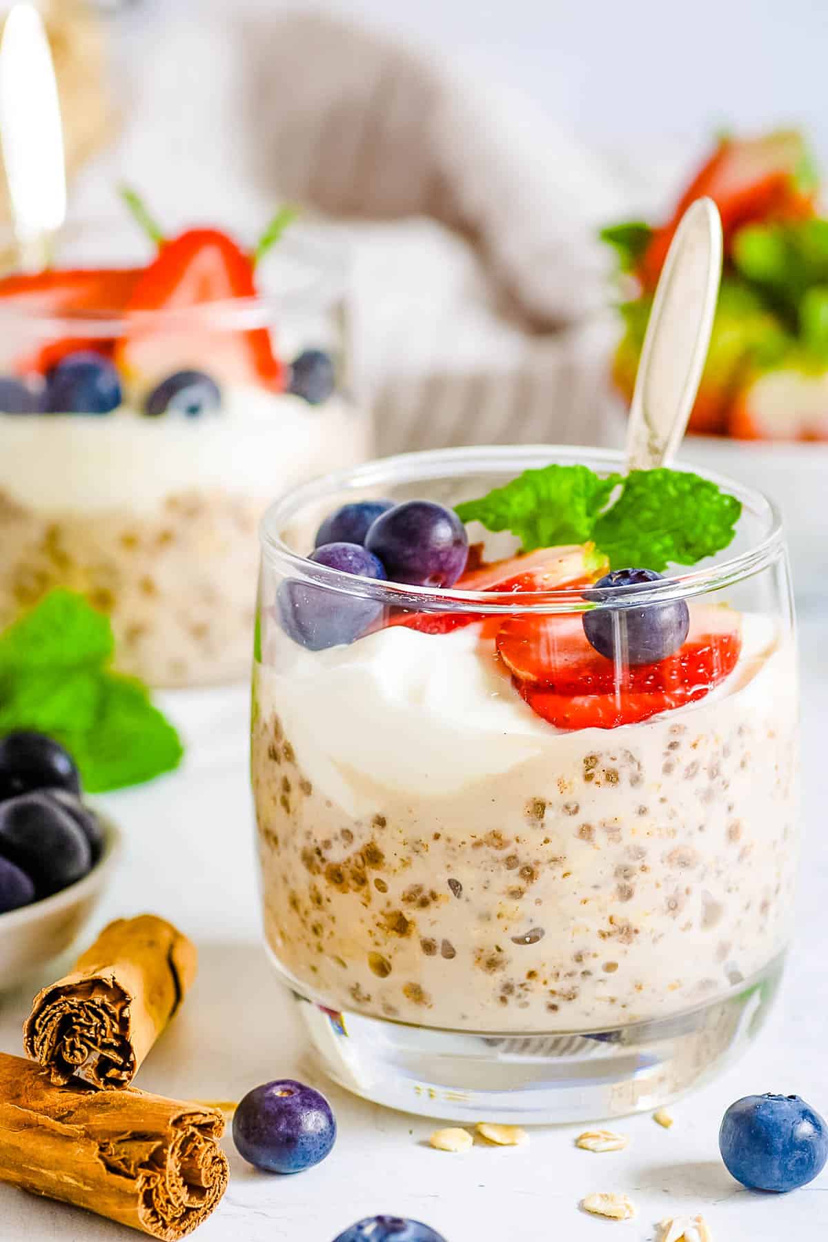 Vegan high protein overnight oats served in gl،es with fresh berries and mint as a garnish.