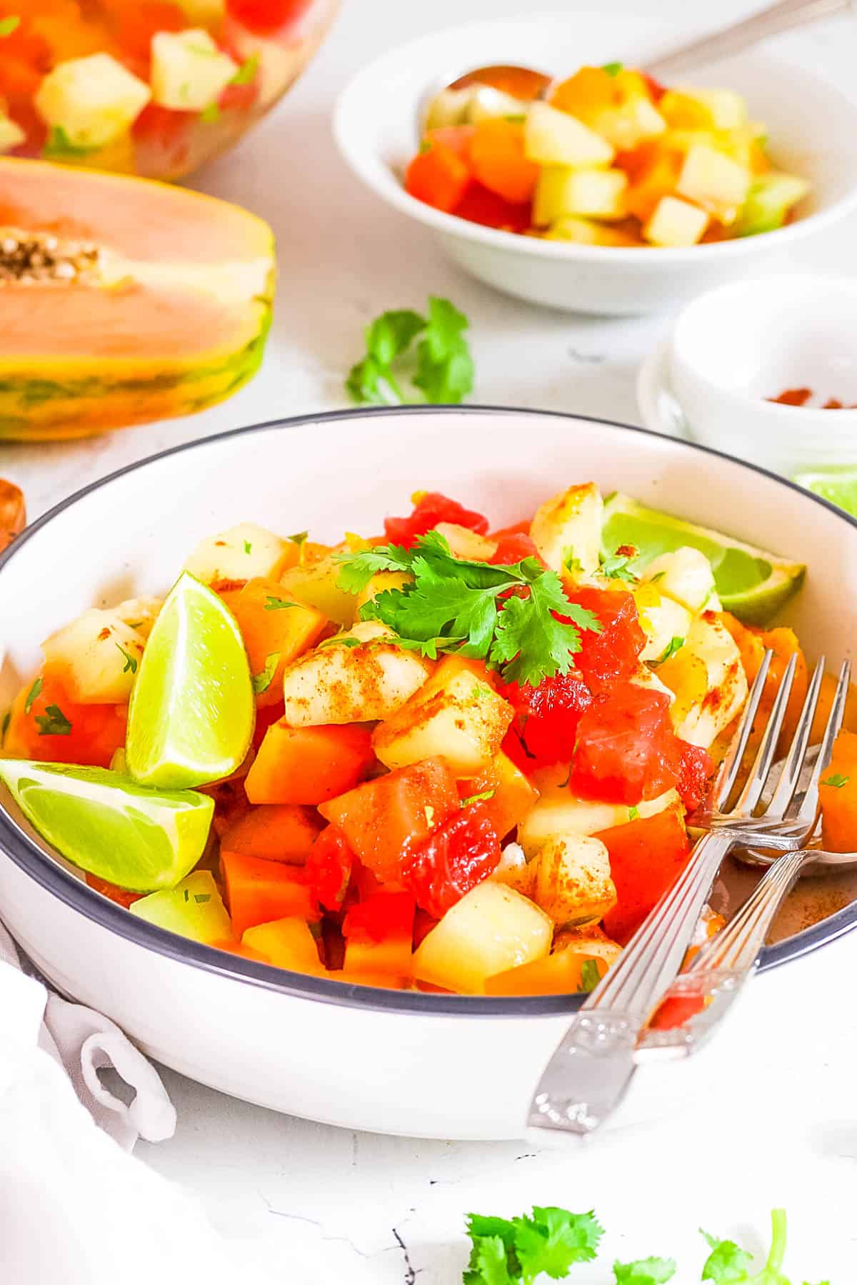 Salade de fruits mexicaine avec assaisonnement chili lime, coriandre et citron vert frais servie dans un bol avec une fourchette.