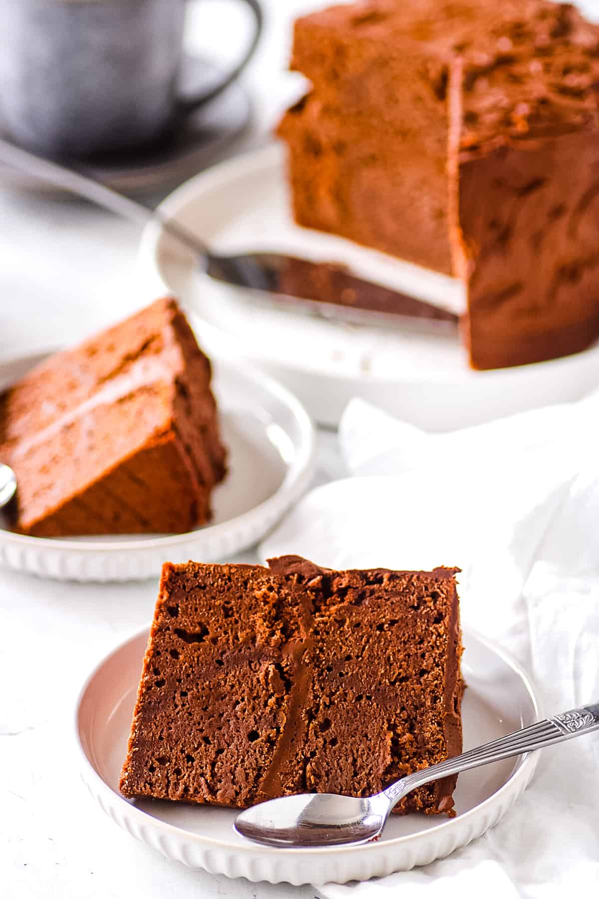 A slice of sugar free chocolate cake, served on a white plate with a spoon.