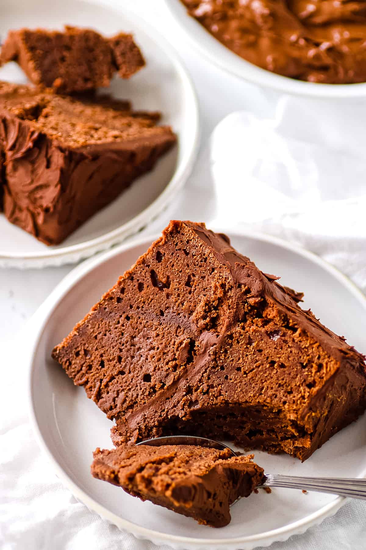 A slice of sugar free chocolate cake, served on a white plate with a spoon.