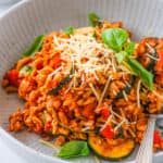 A serving of tofu pasta in a grey bowl garnished with fresh basil and parmesan cheese.