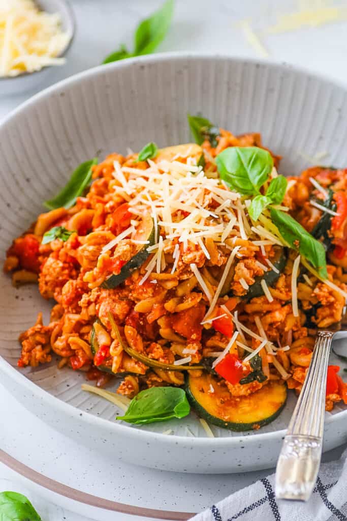 A serving of tofu pasta in a grey bowl garnished with fresh basil and parmesan cheese.
