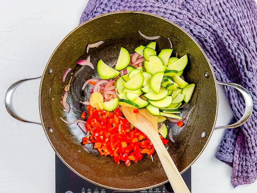Sliced fresh vegetables in a large wok or pan being sautéed.