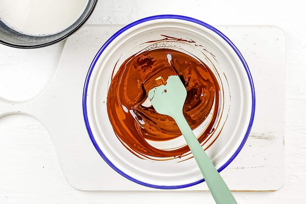 A large mixing bowl with melted chocolate being mixed with a spatula. 