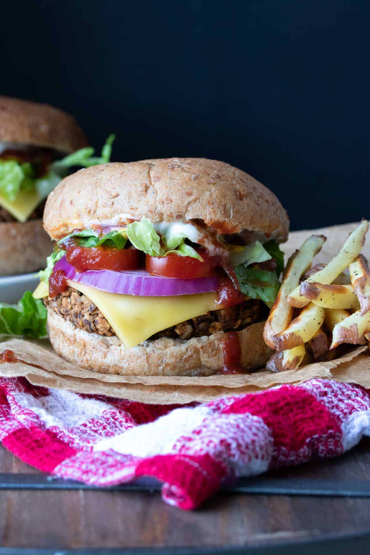 An easy lentil veggie burger recipe that uses up any veggies you have hanging around. It's flavorful, has a great texture and can even be made gluten-free! #veganburger #easyveganrecipes A fully loaded veggie burger on a bun next to a pile of fries