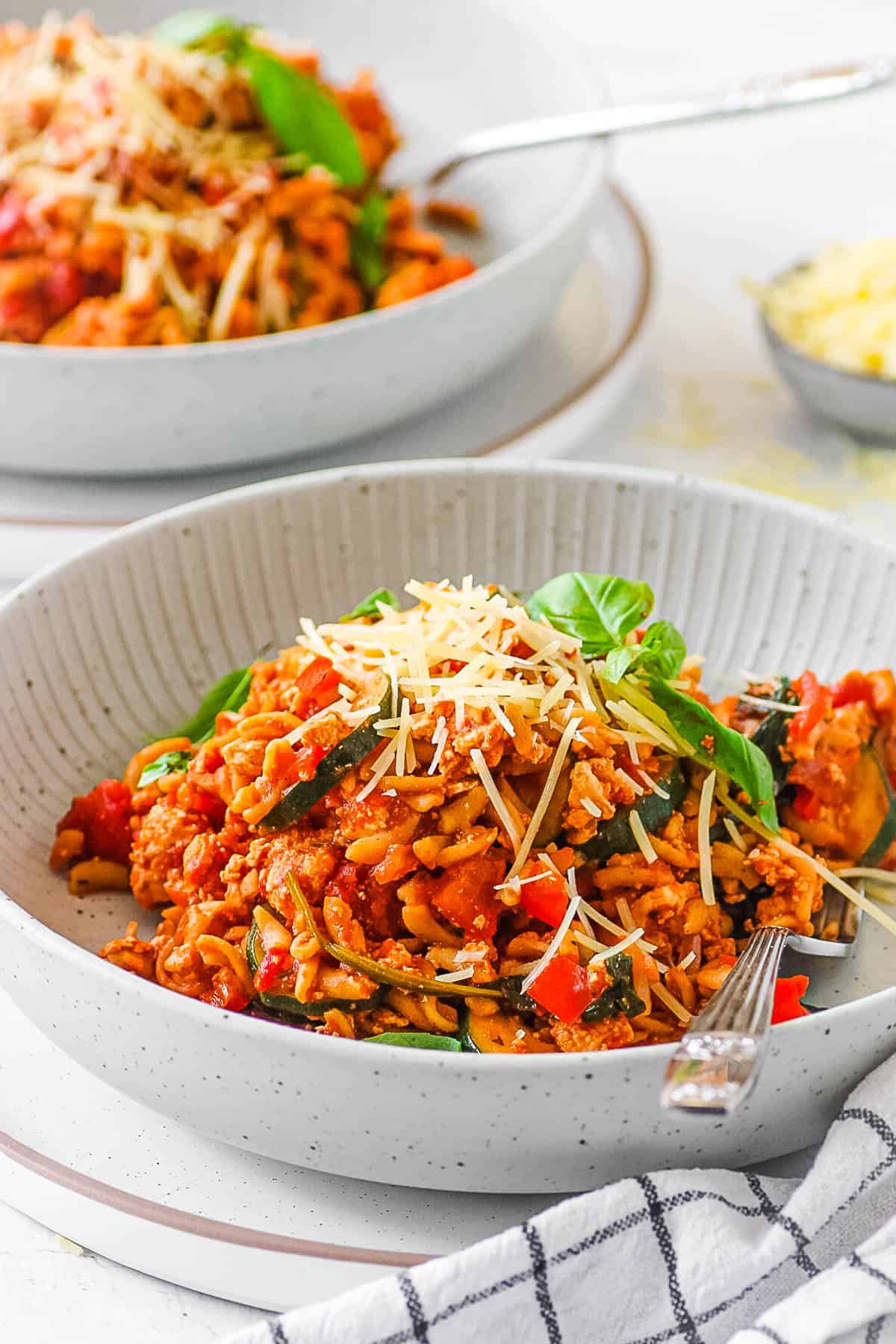 A serving of tofu pasta in a grey bowl garnished with fresh basil and parmesan cheese.